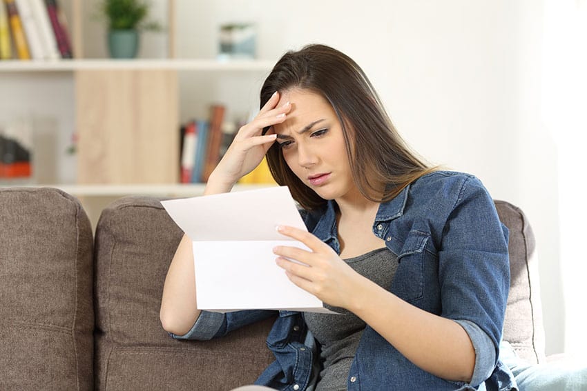 A woman holding a Benefits Claim document seated on a couch.